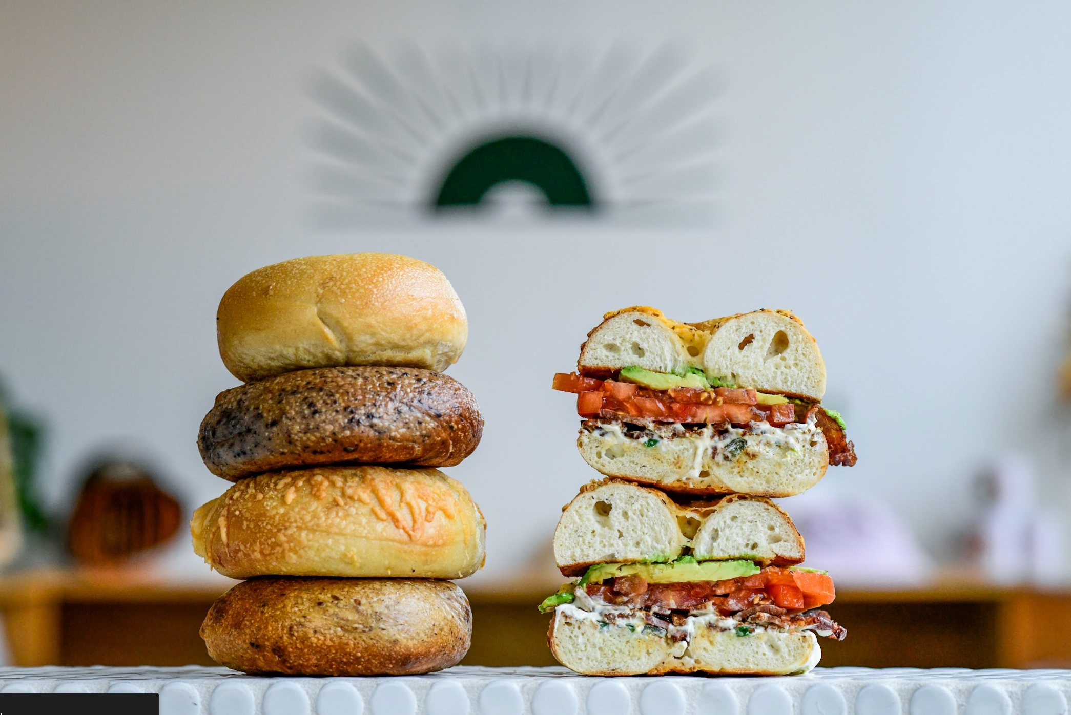 A stack of fresh Rosen's bagels next to two stacked bagel sandwiches